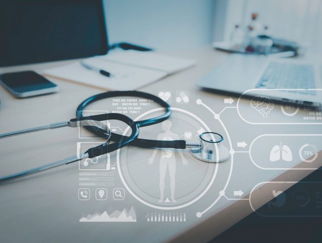 A stethoscope resting on a desk next to a laptop and a smartphone; an illustration of modern healthcare technology.