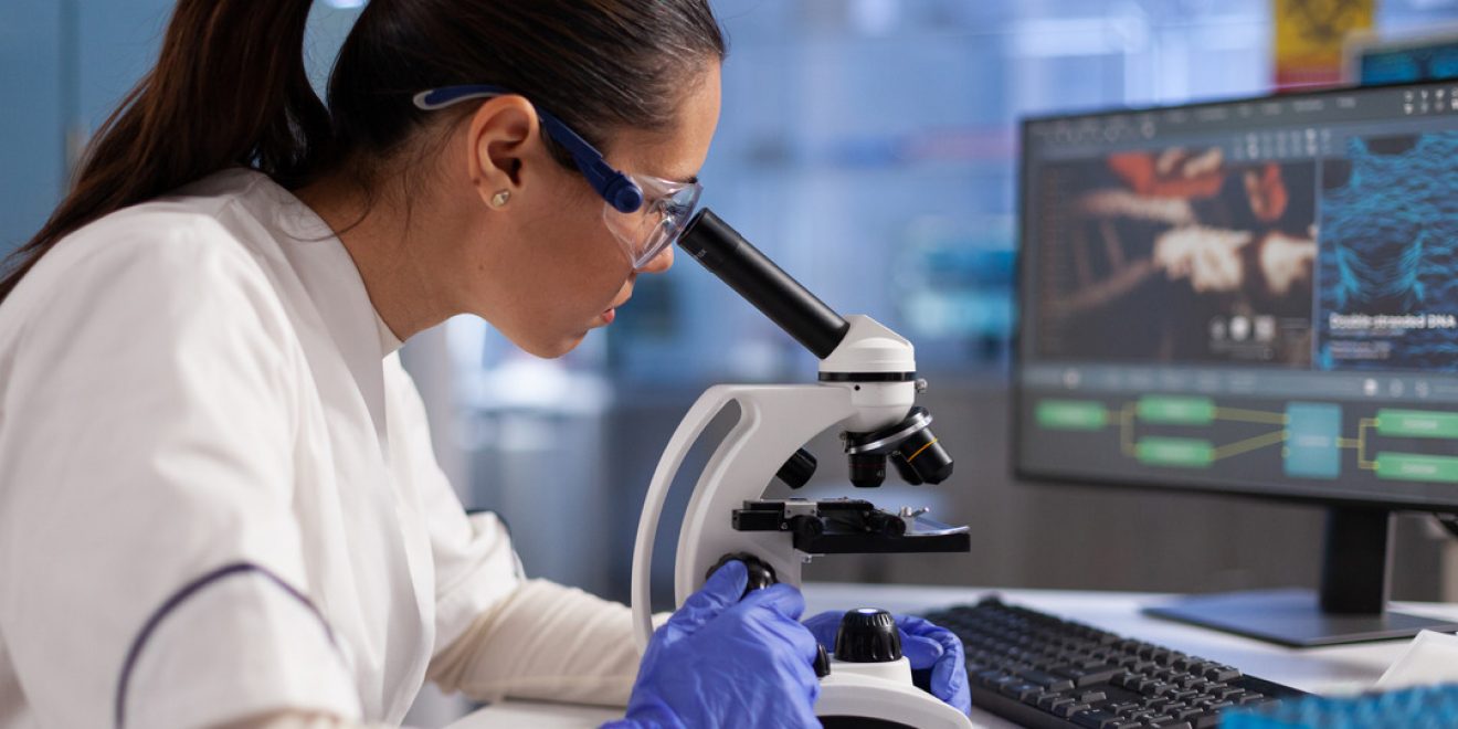 A woman in lab coat conducting microscope analysis. Visual for clinical trials management.