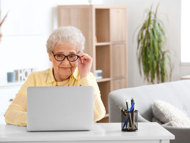 An older woman seated at a desk with a laptop, participating in online therapy