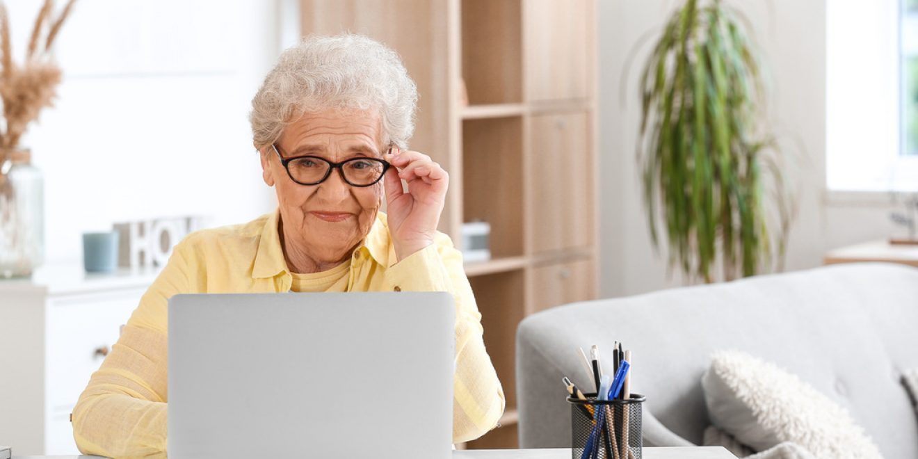 An older woman seated at a desk with a laptop, participating in online therapy