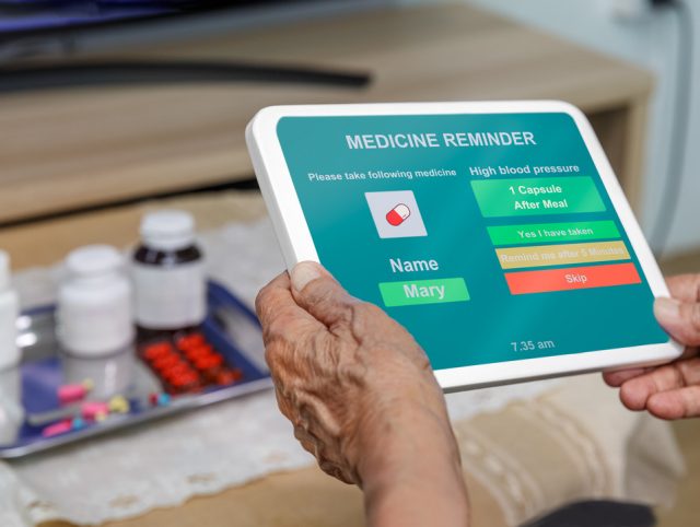 An older adult using a tablet to check medication reminders, showcasing technology aiding with dementia care.