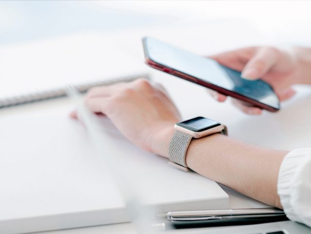 A person at a desk with a phone and a watch, demonstrating the use of wearable technology.