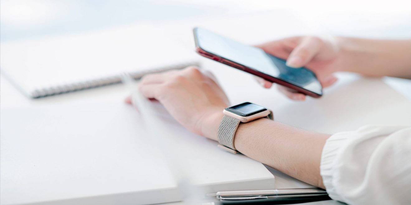 A person at a desk with a phone and a watch, demonstrating the use of wearable technology.